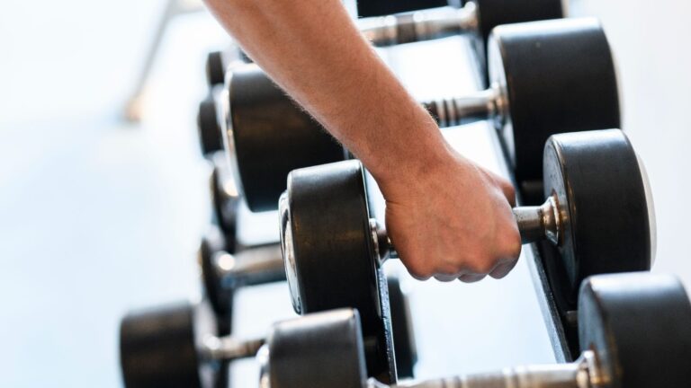 Hand gripping a dumbbell on a weight rack