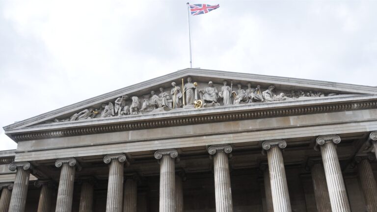 The British Museum's stone pediment and columns beneath a Union flag in London.